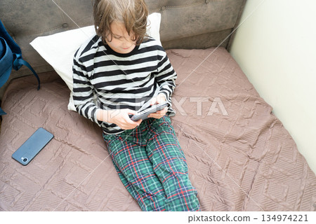 Boy in pajamas using a tablet computer on the bed. Child relaxing at home with a device 134974221