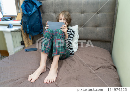 Child in pajamas using a digital tablet in bed. Boy relaxing at home with a gadget 134974223