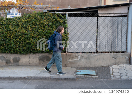 A young boy with a backpack walks to school on a city sidewalk. Student commuting 134974230
