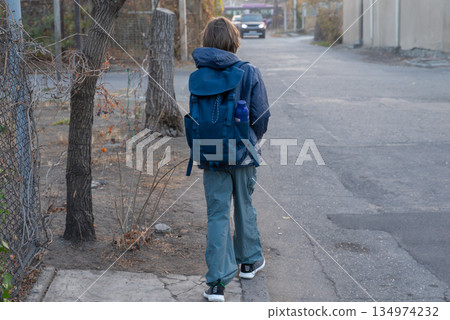 A student with a backpack walking away from the camera. Back view of a boy on a city street 134974232