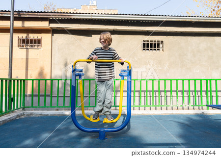 Happy boy exercising on an outdoor fitness machine. Active child in a public park playground 134974244