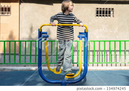 Young boy playing on outdoor exercise equipment. Active child on a playground air walker 134974245