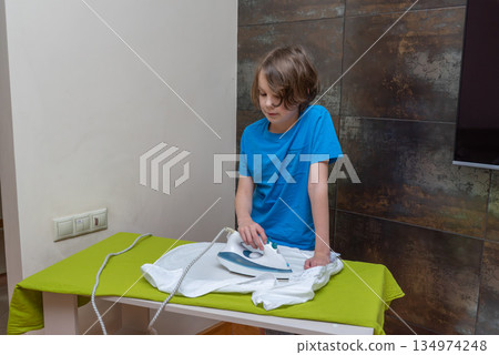 Young boy ironing a white shirt at home. Child helping with household chores and laundry Young boy ironing a white shirt at home. Child helping with household chores and laundry 134974248