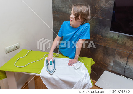 Young boy ironing a white shirt at home. Child learning household chores and life skills Young boy ironing a white shirt at home. Child learning household chores and life skills 134974250