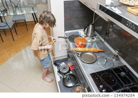 A young boy searching for cookware in an open kitchen drawer. Child helping at home 134974284