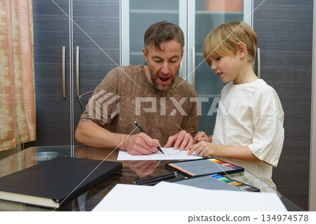 Dad and son drawing together at a desk. Homeschooling and parenting concept Dad and son drawing together at a desk. Homeschooling and parenting concept 134974578