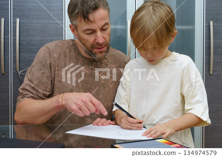 A father helps his young son with a drawing lesson at home. Parent teaching a child creative skills A father helps his young son with a drawing lesson at home. Parent teaching a child creative skills 134974579