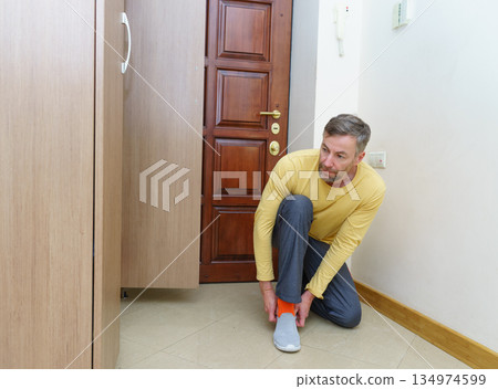 Middle-aged man putting on casual shoes in a home entryway. Getting ready to leave the house Middle-aged man putting on casual shoes in a home entryway. Getting ready to leave the house 134974599