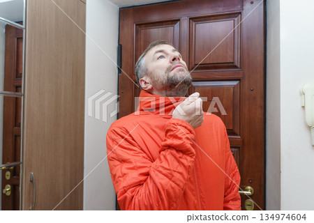 Middle-aged man in a bright orange jacket looking up inside a home entryway. Getting ready to go out Middle-aged man in a bright orange jacket looking up inside a home entryway. Getting ready to go out 134974604