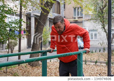 Middle-aged man doing dips on parallel bars. Outdoor fitness workout in autumn Middle-aged man doing dips on parallel bars. Outdoor fitness workout in autumn 134974606