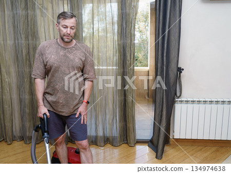 A middle-aged man doing household chores with a vacuum cleaner. Cleaning the floor at home 134974638