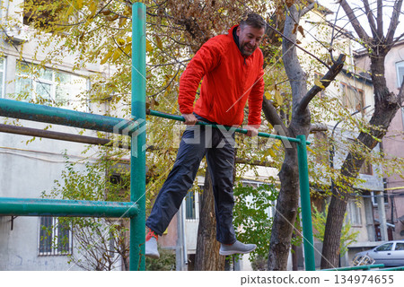 Active middle-aged man doing a muscle-up on a horizontal bar. Outdoor fitness training in autumn 134974655