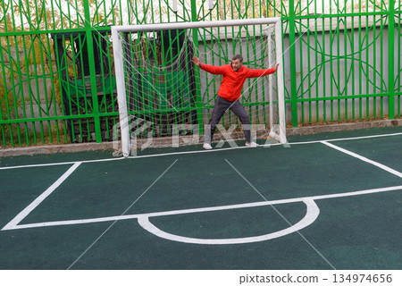 Active middle-aged man defending a soccer goal. Goalkeeper training on an outdoor sports field Active middle-aged man defending a soccer goal. Goalkeeper training on an outdoor sports field 134974656