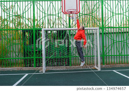 Man jumping to a basketball hoop on an outdoor court. Athlete playing inside a soccer goal Man jumping to a basketball hoop on an outdoor court. Athlete playing inside a soccer goal 134974657
