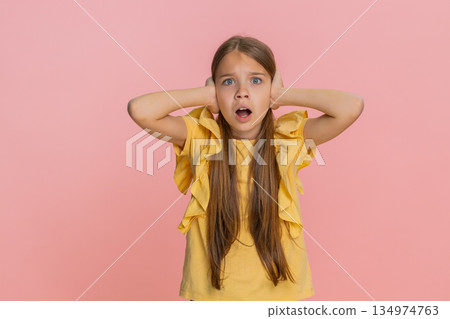 Child girl kid covers ears with hands opens eyes wide showing fear or panic from loud noise or sound 134974763