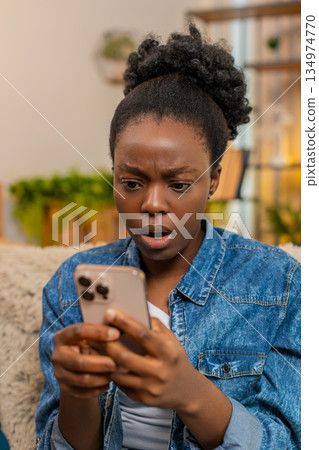 African American young woman angry texting on smartphone during online social media chat at home 134974770