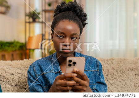 African American young woman angry texting on smartphone during online social media chat at home African American young woman angry texting on smartphone during online social media chat at home 134974771