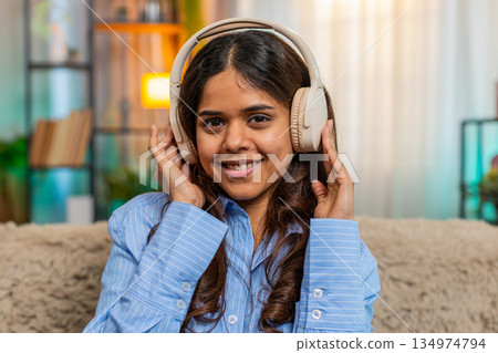 Indian woman listening to music with wireless headphones at home, smiling and moving head with joy Indian woman listening to music with wireless headphones at home, smiling and moving head with joy 134974794