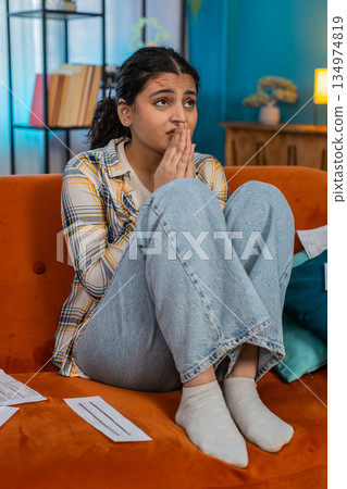 Indian woman praying sitting on sofa looking upward asking help holding documents hoping for miracle Indian woman praying sitting on sofa looking upward asking help holding documents hoping for miracle 134974819