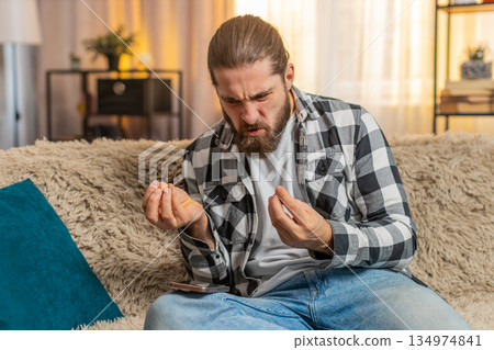 Young man anxious at home, urgent phone call on knee, frustration, loud speaker, intense quarrel Young man anxious at home, urgent phone call on knee, frustration, loud speaker, intense quarrel 134974841