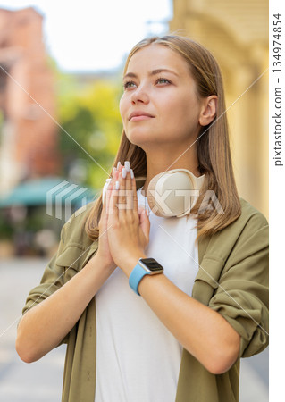 Young Caucasian woman meditating, breathes deeply with hands clasped, praying eyes closed on street 134974854