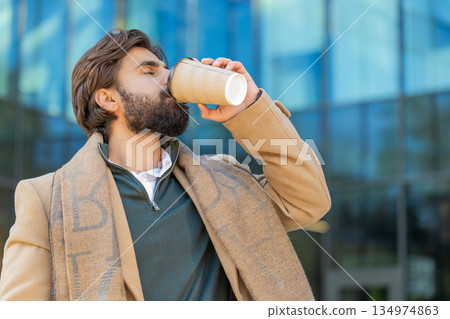 Happy Indian business man tourist enjoying morning coffee hot drink walking on city downtown street 134974863