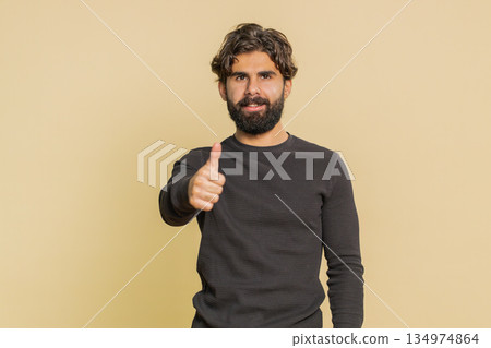 Happy man raises thumbs up agrees with something, and gives positive reply against beige background Happy man raises thumbs up agrees with something, and gives positive reply against beige background 134974864