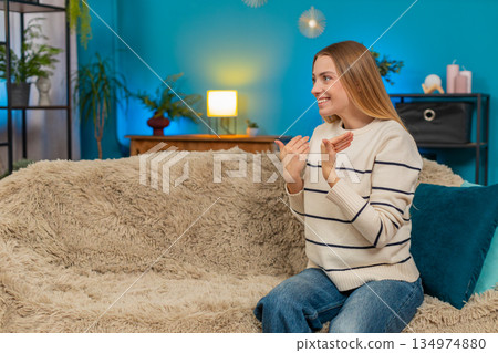 Caucasian woman conversing with imaginary friend, laughing, making air hug gesture at home on sofa Caucasian woman conversing with imaginary friend, laughing, making air hug gesture at home on sofa 134974880