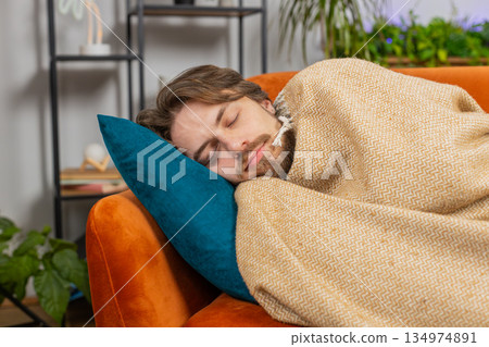 Tired young man lying down on comfortable couch, taking a rest, daytime nap relaxing falling asleep 134974891