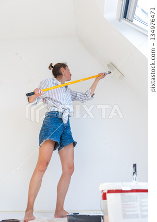 Portrait young adult beautiful single happy woman painting wall paint roller brush white color living room moving new home flat . Female painter decorating interior renovation residential apartment 134976471