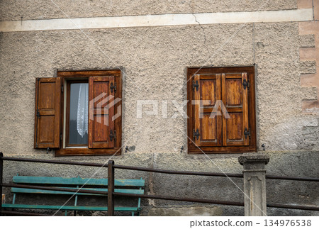 Rustic house facade with wooden shutters and bench in mountain village Rustic house facade with wooden shutters and bench in mountain village 134976538