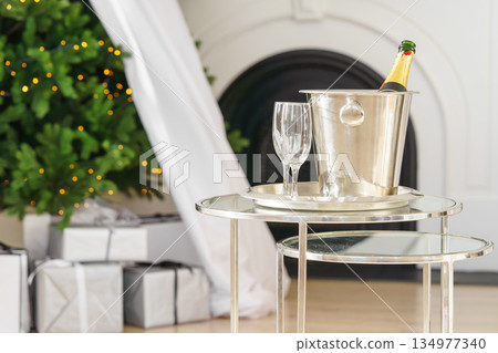 Champagne bottle in ice bucket with glasses on glowing Christmas tree lights with gifts background 134977340
