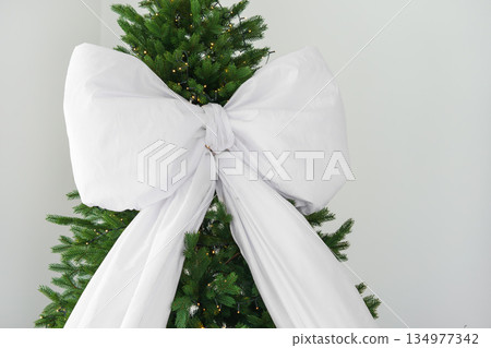 Lush green Christmas tree with trendy modern large white bow festive decoration for indoor holidays 134977342