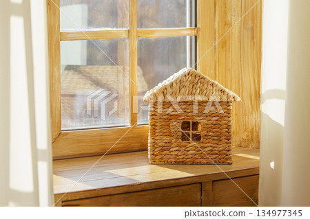 Small woven house model on sunny wooden window sill against natural light window in child room Small woven house model on sunny wooden window sill against natural light window in child room 134977345