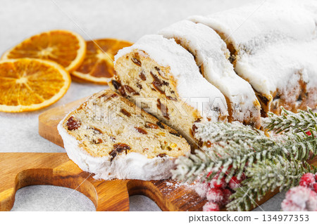 Traditional sliced Christmas stollen loaf with raisins and powdered sugar on wooden cutting board 134977353