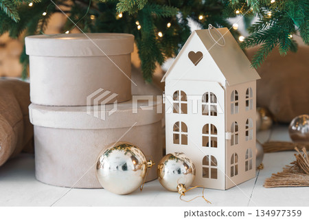 Cozy Christmas decor with round white gift boxes and decorative house under festive fir tree Cozy Christmas decor with round white gift boxes and decorative house under festive fir tree 134977359