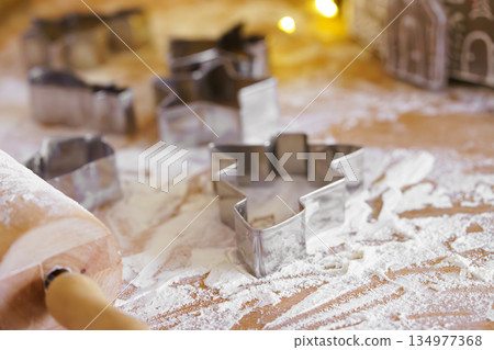 Baking gingerbread cookie cutters, wooden rolling pin, and flour are messily spread on kitchen table Baking gingerbread cookie cutters, wooden rolling pin, and flour are messily spread on kitchen table 134977368