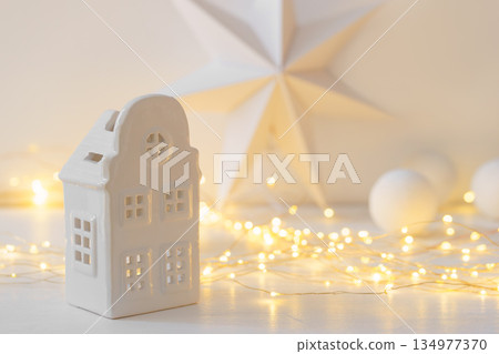 Minimalist Christmas decor, ceramic house on garland warm festive fairy lights background Minimalist Christmas decor, ceramic house on garland warm festive fairy lights background 134977370