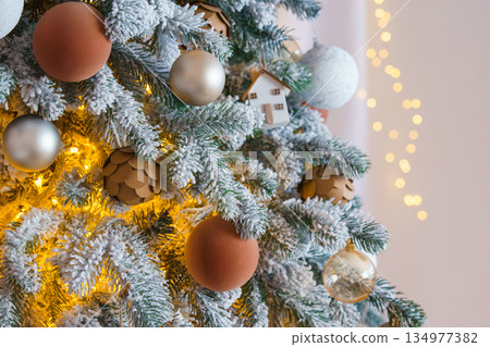 Snowy Christmas tree branch with baubles ornament and warm golden holiday light illumination 134977382