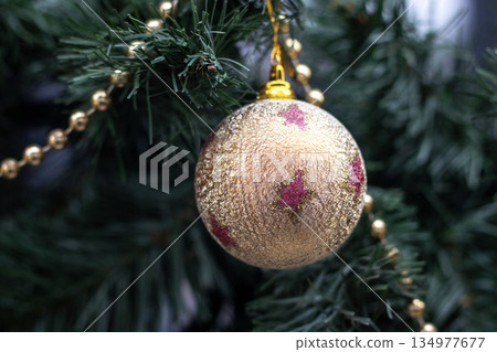 Golden Christmas ornament on a pine tree with glitter and beaded garland in festive decoration 134977677