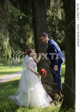 Groom helping bride climb tree stump surrounded by forest 134977679