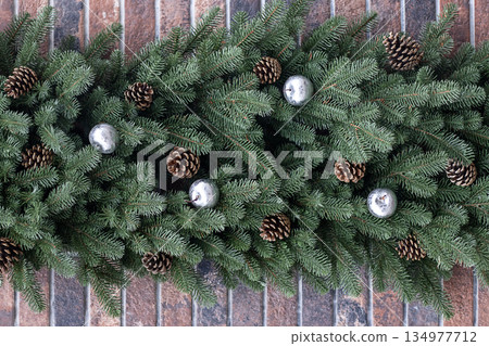 Festive evergreen garland with pinecones and silver ornaments on a rustic brick background 134977712
