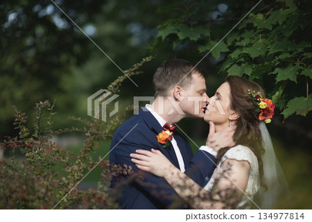 Groom and bride sharing gentle kiss under green foliage 134977814