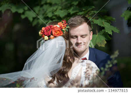 Bride resting on groom shoulder enjoying gentle moment under trees 134977815