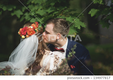 Bride and groom embracing closely beneath canopy of green leaves 134977817