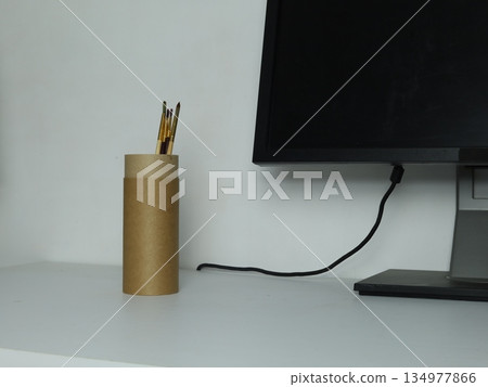 Cup filled with paint brushes standing on a creative workspace desk near a computer. 134977866