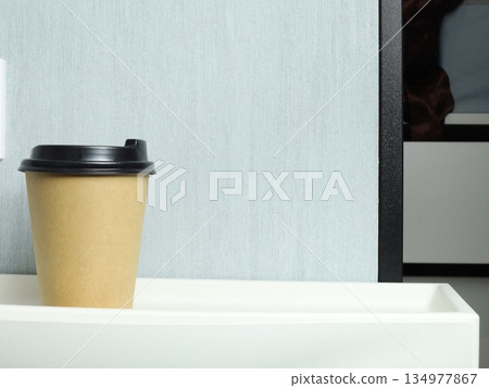 Craft paper coffee cup standing on a dresser in a minimalist interior. 134977867