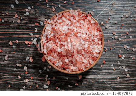 Wooden bowl filled with pink Himalayan salt crystals on dark wooden table, natural mineral seasoning for healthy cooking and spa concepts. 134977972