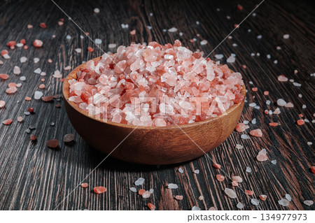 Wooden bowl filled with pink Himalayan salt crystals on dark wooden table, natural mineral seasoning for healthy cooking and spa concepts. 134977973