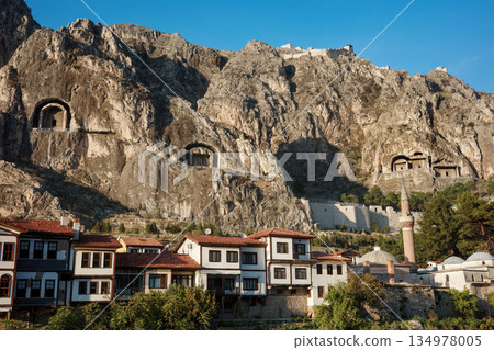 Ancient rock-cut tombs carved in cliff face above Amasya city with traditional Ottoman houses, mosque with minaret below in valley, heritage and historical architecture concept 134978005